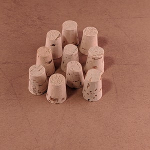 May include: A collection of eleven natural cork bottle stoppers arranged on a brown surface. The stoppers are cylindrical with a flat top and a textured, light brown appearance, suggesting a wine-related theme.