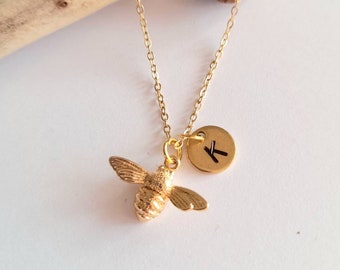 May include: Gold bee charm necklace with a gold initial disc charm. The initial disc has the letter 'K' engraved on it.