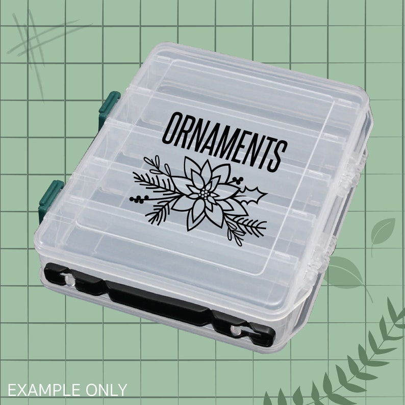May include: Clear plastic storage box with a black label that says "ORNAMENTS" and a black silhouette of a poinsettia flower.