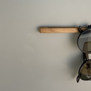 Könnte beinhalten: Ein Holzregal mit einer schwarzen Sonnenbrille, die daran hängt.