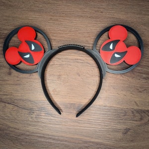 May include: Black headband with red and black Mickey Mouse ears featuring a Deadpool design.