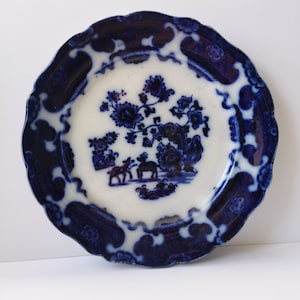 May include: A blue and white porcelain plate with a floral design and a scene of two deer in a forest. The plate has a scalloped edge.