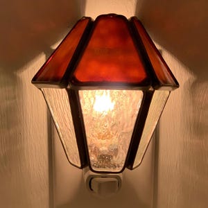 May include: A red stained glass nightlight with a clear glass base and a white on/off switch. The nightlight is plugged into a standard electrical outlet.