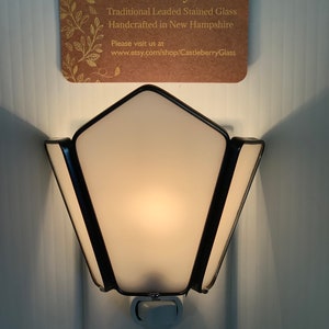 May include: A black and white nightlight with a frosted glass shade in the shape of a star. The nightlight is plugged into an outlet. The text on the card reads "Castleberry Glass Traditional Leaded Stained Glass Handcrafted in New Hampshire Please visit us at www.etsy.com/shop/CastleberryGlass"