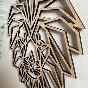 May include: Geometric wooden lion head wall art with a black outline. The lion's mane is made up of many triangles and the face is detailed with eyes, nose, and mouth.