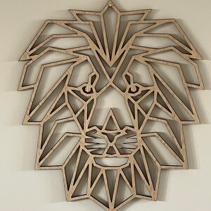 May include: Geometric wooden lion head wall decor. The lion's face is made up of triangles and other geometric shapes. The wood is a light brown color.