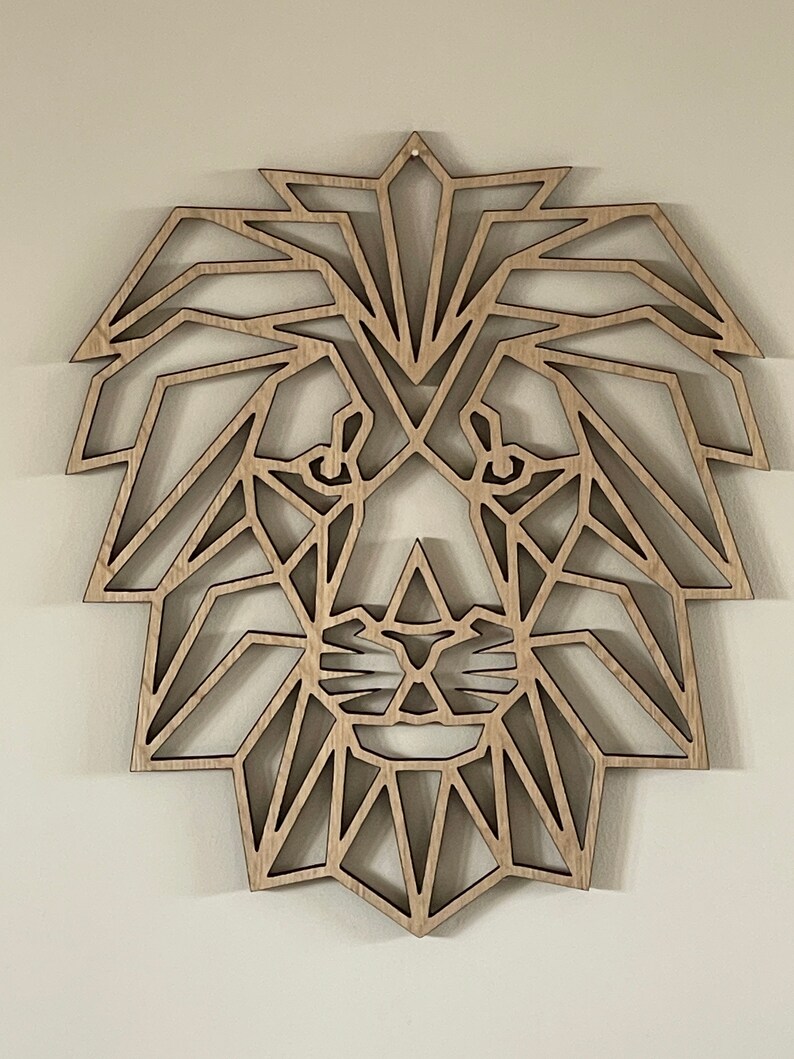 May include: Geometric wooden lion head wall decor. The lion's face is made up of triangles and other geometric shapes. The wood is a light brown color.
