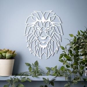 May include: White geometric lion head wall decor. The lion's mane is made up of many triangles. The lion's face is detailed with a nose, eyes, and mouth.
