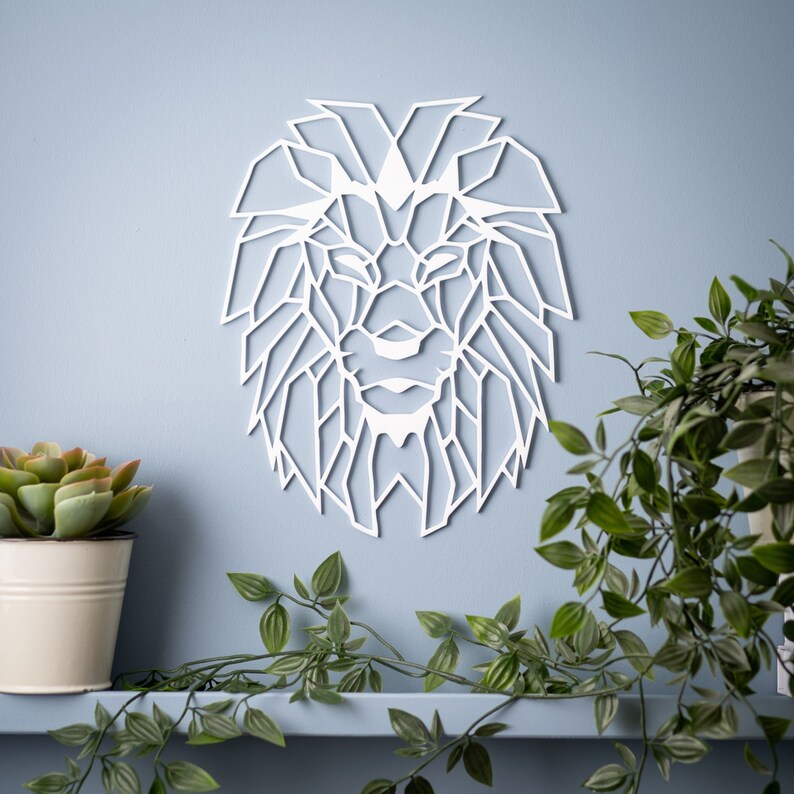 May include: White geometric lion head wall decor. The lion's mane is made up of many triangles. The lion's face is detailed with a nose, eyes, and mouth.