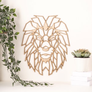 May include: Geometric wooden lion head wall decor. The lion's face is made up of many triangles and lines, creating a modern and abstract look. The wood is a light brown color.