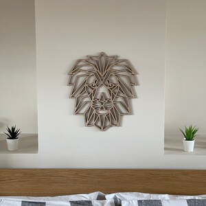 May include: A geometric wooden lion head wall decor in a light brown color. The lion head is made of many triangles and is mounted on a white wall above a bed with a black and white checkered bedspread.