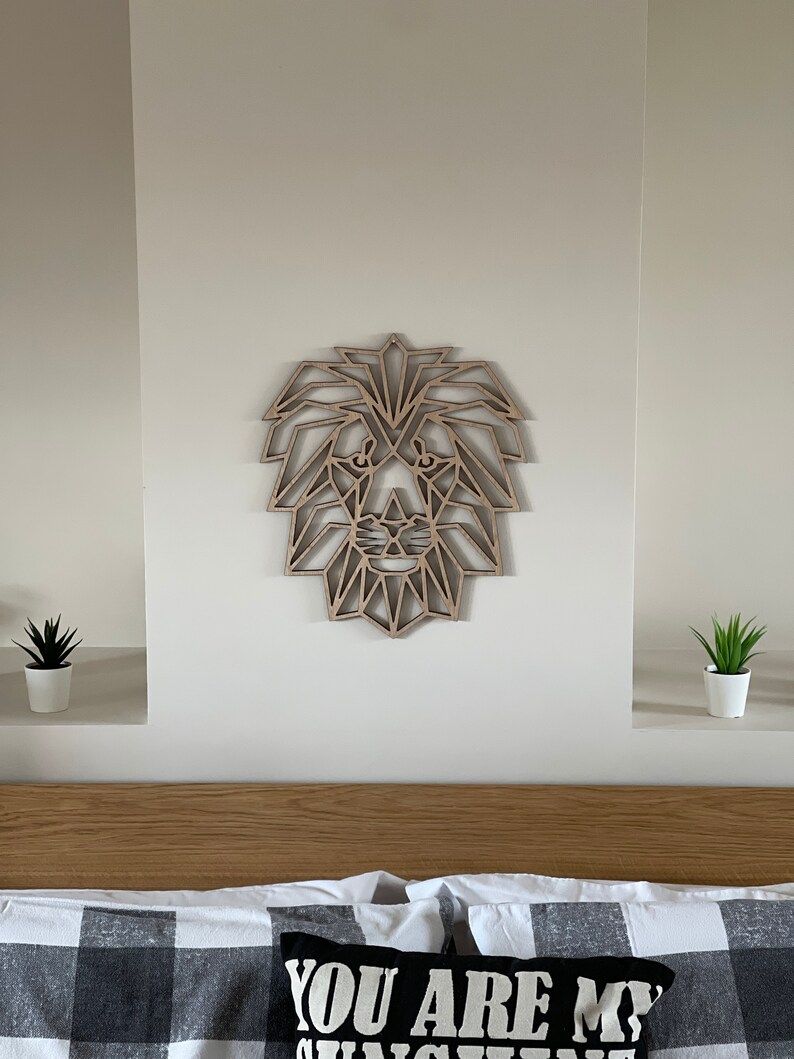 May include: A geometric wooden lion head wall decor in a light brown color. The lion head is made of many triangles and is mounted on a white wall above a bed with a black and white checkered bedspread.
