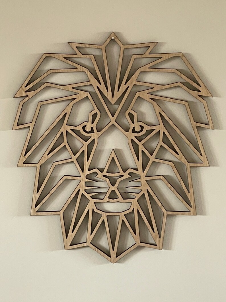 May include: Geometric wooden lion head wall decor. The lion's mane is made up of intricate triangles and the face is detailed with a nose and eyes.