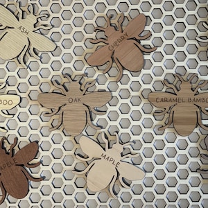 May include: Nine wooden bee ornaments in various wood types, including ash, cherry, oak, maple, walnut, and bamboo. Each bee has a different wood grain pattern and is labeled with the type of wood.