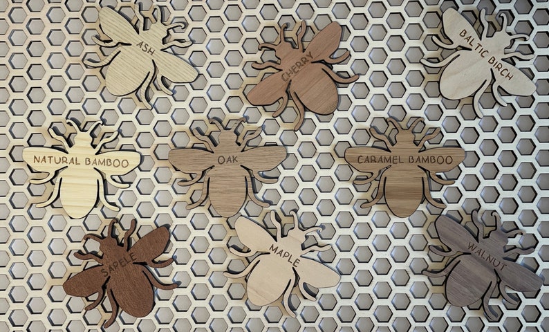 May include: Nine wooden bee ornaments in various wood types, including ash, cherry, oak, maple, walnut, and bamboo. Each bee has a different wood grain pattern and is labeled with the type of wood.