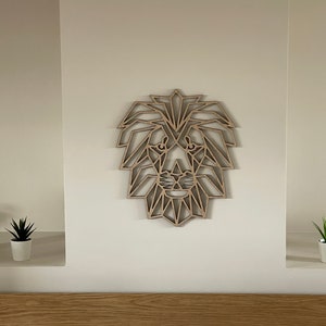 May include: A geometric wooden lion head wall decor in a light brown color. The lion head is made of many small triangles and is mounted on a white wall.
