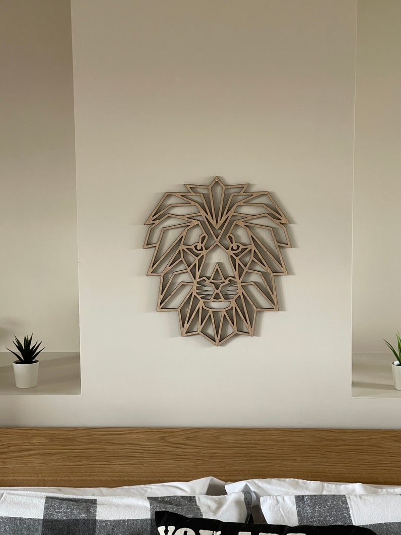 May include: A geometric wooden lion head wall decor in a light brown color. The lion head is made of many small triangles and is mounted on a white wall.