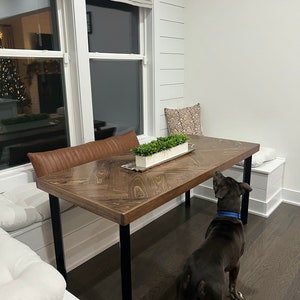 May include: A dark brown wooden table with black metal legs, a white cushion bench, and a black dog standing next to the table.