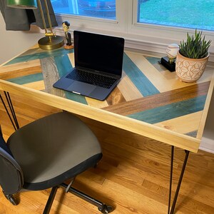 May include: A wooden desk with a chevron pattern top in shades of blue, brown, and beige. The desk has black hairpin legs and a laptop computer is sitting on the surface.