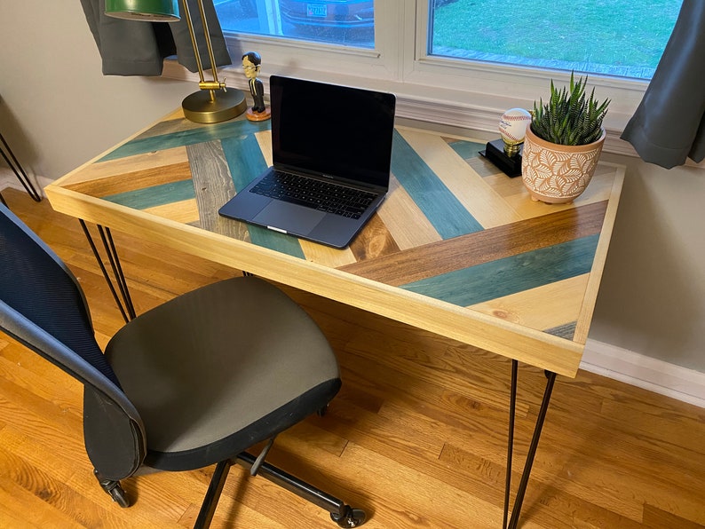 May include: A wooden desk with a chevron pattern top in shades of blue, brown, and beige. The desk has black hairpin legs and a laptop computer is sitting on the surface.