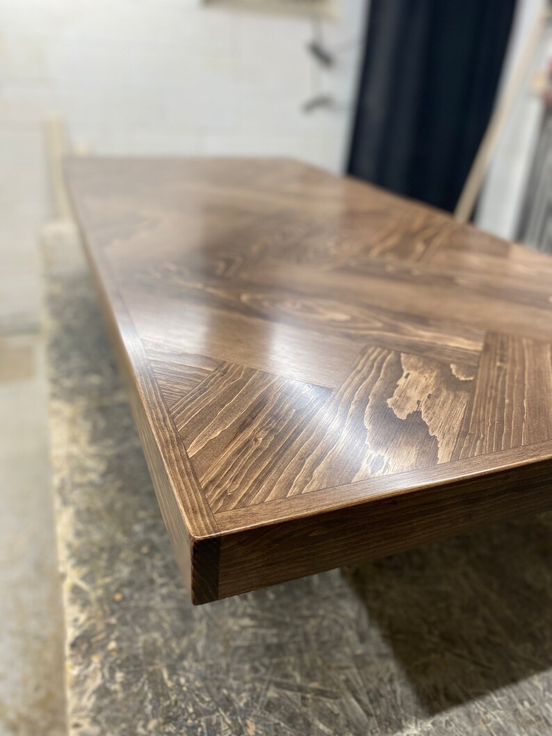 May include: Close-up of a dark brown wooden table top with a herringbone pattern. The table top is smooth and polished, with a slight sheen.