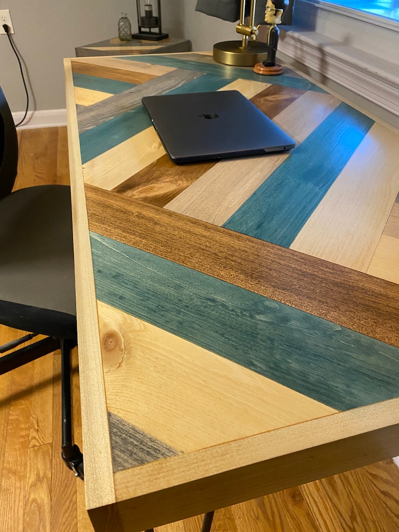 May include: A wooden desk with a chevron pattern in shades of blue, brown, and beige. The desk has a natural wood frame and a laptop computer is sitting on the surface.