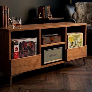 May include: A wooden media console with three open storage compartments. The left section holds a Nirvana vinyl record, the center contains a wooden record player and a Marshall speaker, and the right section holds a Flight of the Conchords record.