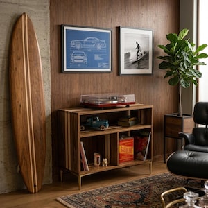 May include: A wooden media console with a dark brown finish and light wood vertical accents, featuring two open shelves, a record player on top, a blue toy truck, books, and a red box labeled GASOLINE stored inside the shelving compartments.