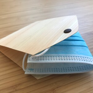 Peut inclure: Un masque facial bleu clair plié et rangé dans un étui en bois avec une fermeture à bouton marron.