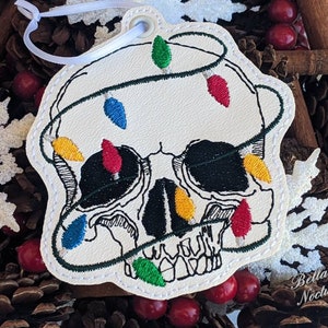 May include: White felt Christmas ornament shaped like a skull with a string of colorful lights wrapped around it. The lights are red, green, blue, and yellow.