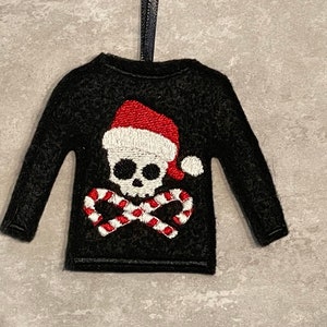 May include: Black felt Christmas ornament shaped like a sweater with a white skull wearing a red Santa hat and candy canes.