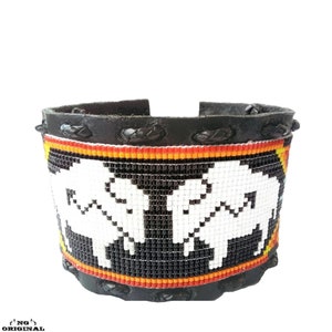 Peut inclure: Un bracelet en cuir noir avec un motif de perles représentant deux buffles blancs sur fond noir. Le travail des perles comprend des accents rouges, orange et jaunes.