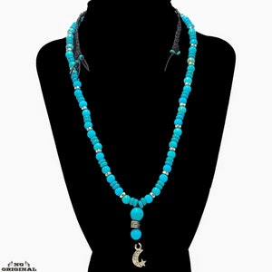 Puede incluir: Collar de cuentas azul turquesa con un colgante de media luna de plata. El collar está en un maniquí negro.