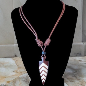 Op de afbeelding: Een bruine en witte pijlpunt hanger ketting. De hanger heeft een donkerbruine houten basis met witte chevron ontwerpen. De ketting heeft een lichtbruin leren koord met een geknoopt ontwerp en een kleine blauwe kraal.
