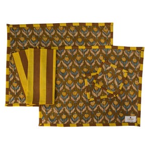 Pu&ograve; includere: Un set di tovagliette, tovaglioli e sottobicchieri verde oliva. Le tovagliette e i sottobicchieri presentano un motivo floreale giallo e blu, con un bordo giallo e marrone. I tovaglioli sono a righe gialle e marroni.