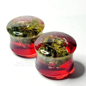 May include: Two double flare ear plugs with a ruby red base and a green and brown interior. The plugs are 12.7mm in size and have the text "Ruby Red w/Budz".