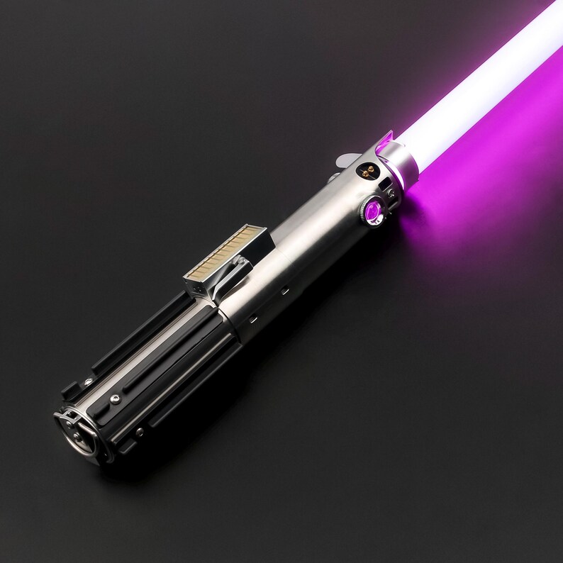 May include: A silver and black lightsaber with a bright purple blade. The hilt has detailed mechanical components, including buttons and a rectangular section. The blade glows brightly against a dark background.