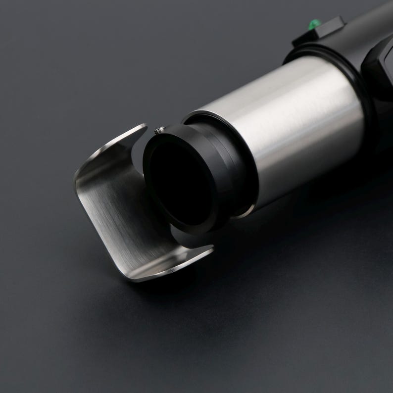 May include: Close-up of a metallic, futuristic device with a black cylindrical component and a curved, silver-colored guard. The device has a sleek, modern design, with a focus on its metallic finish and precision engineering. The background is a dark gray.