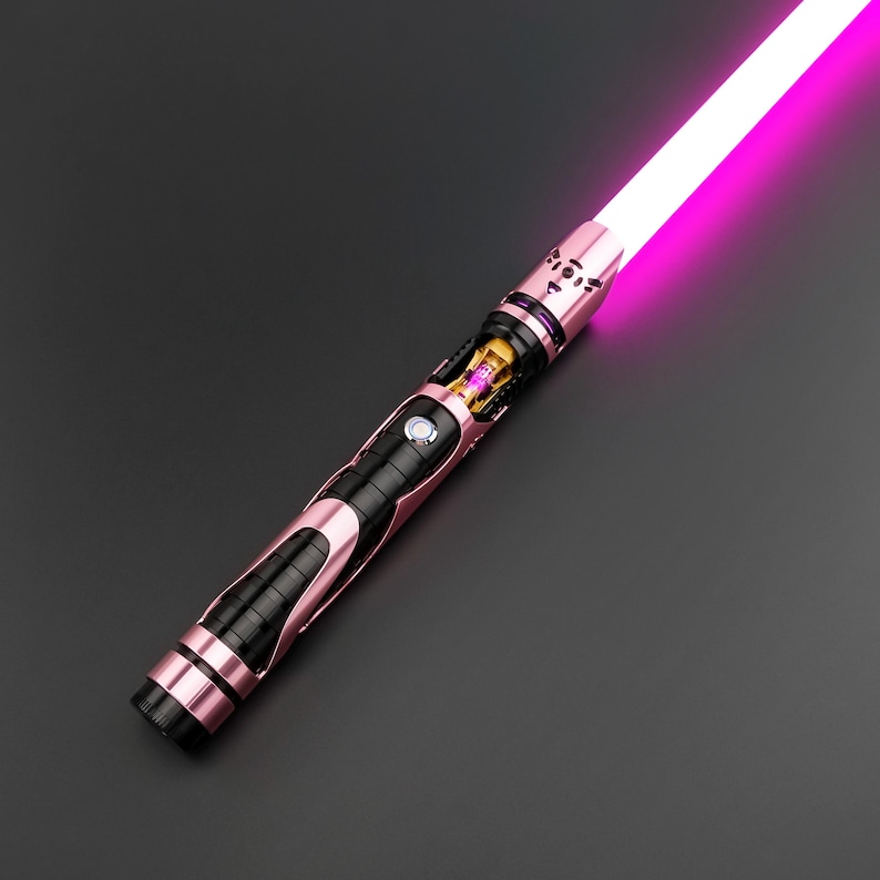 May include: A pink and black lightsaber with a glowing pink blade. The hilt features a metallic pink finish with black accents and intricate detailing. The blade emits a bright pink light, creating a striking contrast against the dark background.