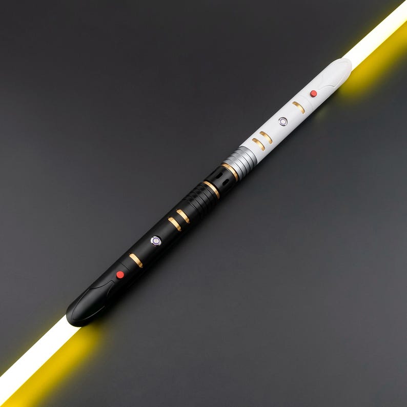 May include: A black and white lightsaber with gold and silver accents. The hilt features red and silver buttons and a yellow blade. The lightsaber is set against a dark gray background.