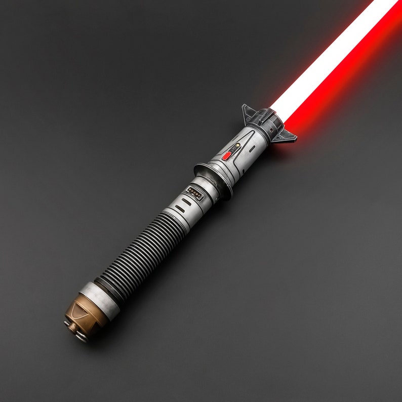 Puede incluir: Un sable de luz plateado con una hoja roja. El sable de luz tiene un agarre texturizado y un mango negro con un bot&oacute;n plateado.