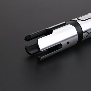 May include: A close-up shot of a silver and black metal tool. It has a cylindrical body and multiple prongs extending from one end. The tool has a polished, reflective surface, suggesting an industrial or mechanical purpose. The background is a solid black.