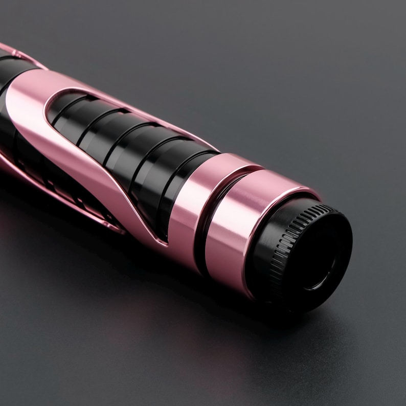 May include: Close-up of a black and rose gold beauty tool. The tool has a cylindrical shape with black ribbed sections and rose gold accents. The end of the tool is black with a textured surface.