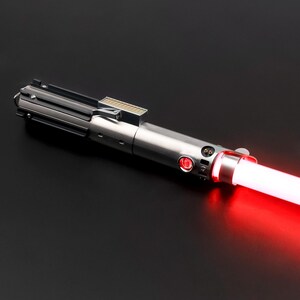 May include: A silver lightsaber with a red glowing blade. The hilt has a detailed design with various buttons and a rectangular section near the top. The blade emits a bright red light, suggesting it is activated.