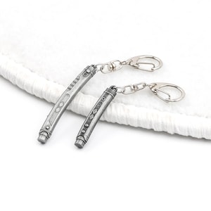 May include: Two silver metal keychains shaped like lightsabers. The keychains are attached to silver key rings.