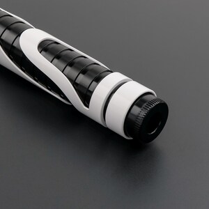 May include: A close-up of a futuristic, black and white lightsaber hilt. The hilt features a black cylindrical core with white accents and a black pommel. The design is sleek and modern, with a focus on geometric shapes.