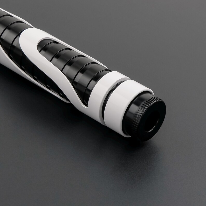 May include: A close-up of a futuristic, black and white lightsaber hilt. The hilt features a black cylindrical core with white accents and a black pommel. The design is sleek and modern, with a focus on geometric shapes.
