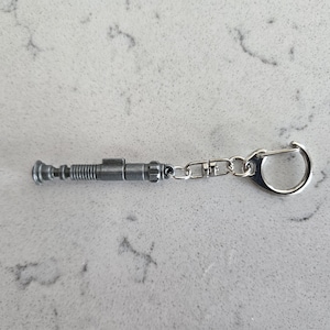 May include: A silver metal keychain featuring a replica of a sonic screwdriver, a fictional tool used in the Doctor Who television series.