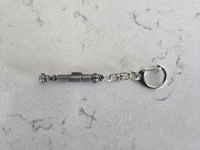 May include: A silver metal keychain featuring a replica of a sonic screwdriver, a fictional tool used in the Doctor Who television series.