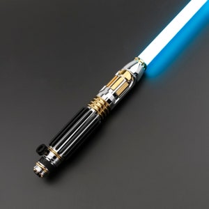 May include: A silver and gold lightsaber with a blue blade. The lightsaber has a black handle with a textured grip.